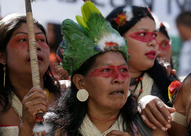 Indigenous people with red face paint and hold signs during a protest in Ecuador.